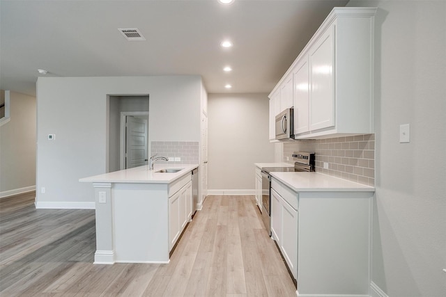 kitchen featuring a peninsula, visible vents, light wood-style floors, light countertops, and appliances with stainless steel finishes