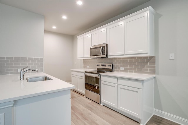 kitchen featuring stainless steel appliances, light countertops, light wood-style floors, white cabinetry, and a sink