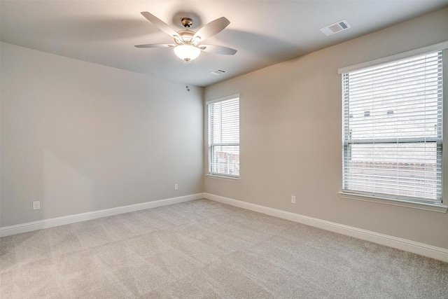 unfurnished room with a ceiling fan, light colored carpet, visible vents, and baseboards