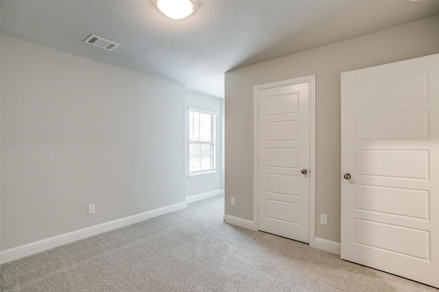 unfurnished bedroom with light carpet, a textured ceiling, visible vents, and baseboards