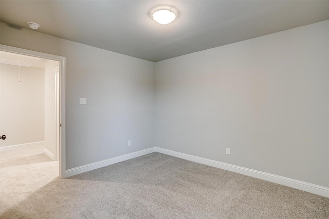 carpeted empty room with attic access and baseboards