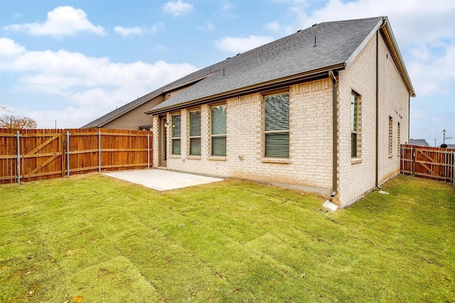 back of property featuring a lawn, a fenced backyard, roof with shingles, a patio area, and brick siding