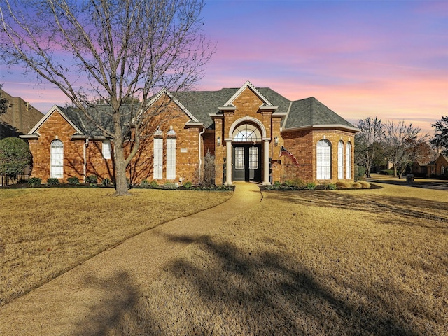 view of front facade with french doors, brick siding, a lawn, and a shingled roof