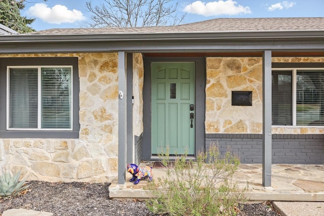 entrance to property featuring stone siding, brick siding, and roof with shingles