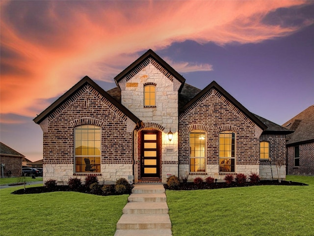 french provincial home featuring brick siding, stone siding, and a front lawn