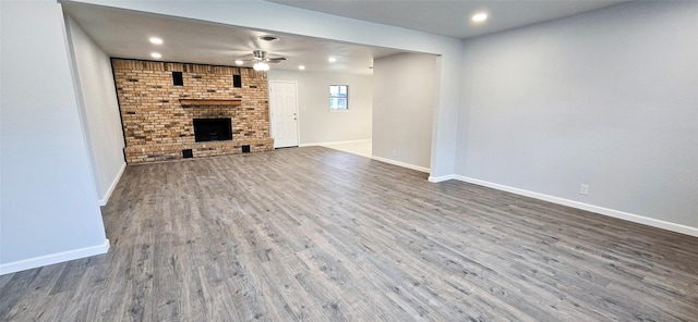 unfurnished living room featuring recessed lighting, a ceiling fan, a brick fireplace, wood finished floors, and baseboards