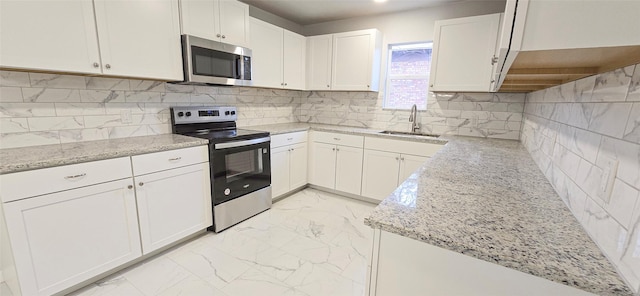 kitchen featuring light stone counters, marble finish floor, stainless steel appliances, white cabinetry, and a sink