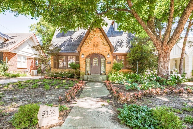 english style home featuring a shingled roof and brick siding