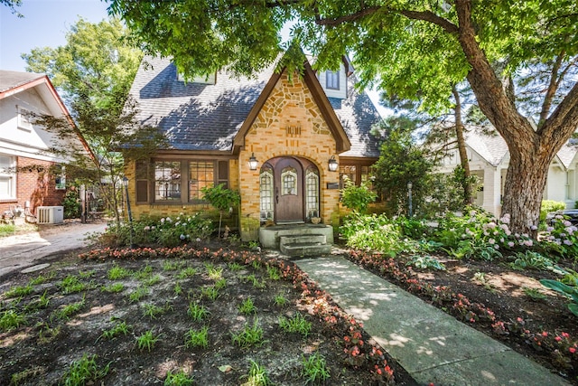 tudor-style house featuring central AC, roof with shingles, and stone siding