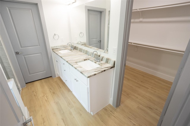 bathroom with double vanity, wood finished floors, a sink, and a walk in closet