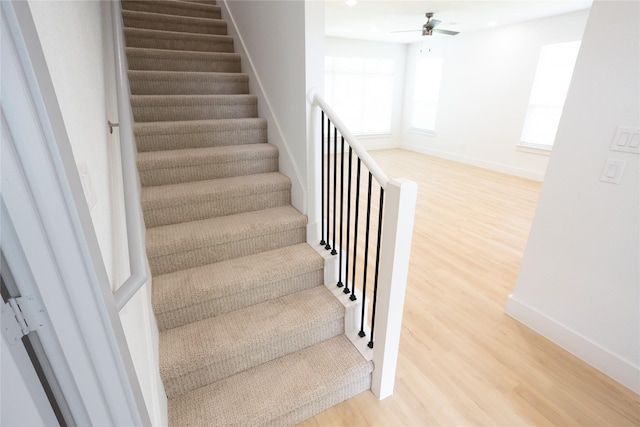 staircase featuring wood finished floors, a ceiling fan, and baseboards