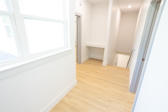 hallway with baseboards, an upstairs landing, and light wood-style floors