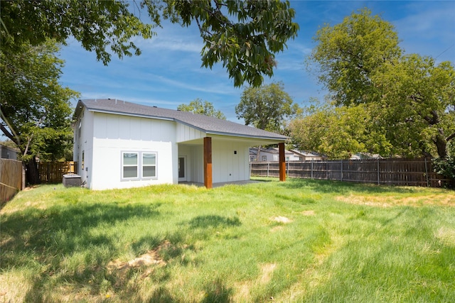 rear view of house featuring board and batten siding, a fenced backyard, central AC, and a yard