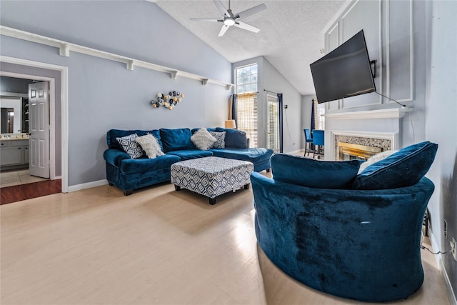 living room featuring ceiling fan, a textured ceiling, wood finished floors, and a glass covered fireplace