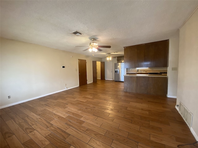 unfurnished living room with dark wood-style floors, ceiling fan, visible vents, and a textured ceiling