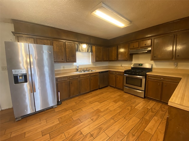 kitchen featuring light wood finished floors, stainless steel appliances, a textured ceiling, under cabinet range hood, and a sink