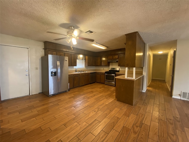 kitchen with light countertops, visible vents, appliances with stainless steel finishes, a peninsula, and under cabinet range hood