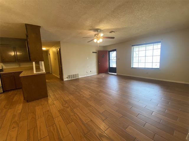 unfurnished living room featuring a ceiling fan, a textured ceiling, visible vents, and dark wood-style flooring