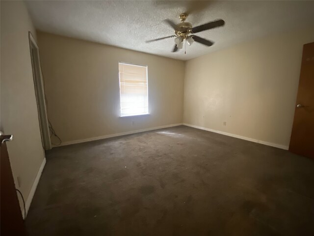 spare room with a textured ceiling, ceiling fan, dark carpet, and baseboards