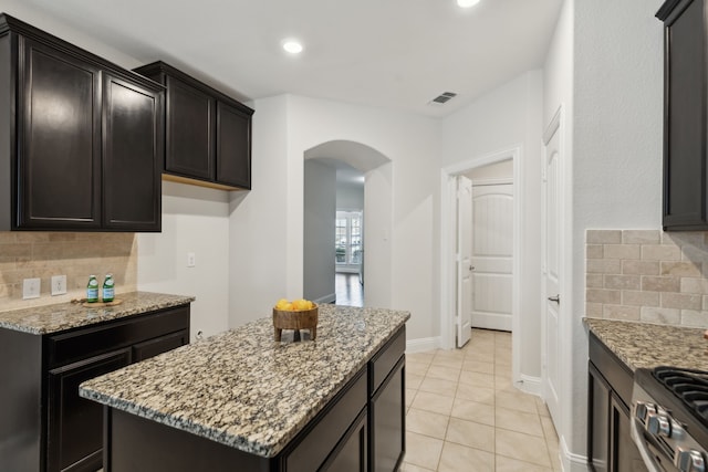 kitchen with visible vents, arched walkways, backsplash, and light stone counters