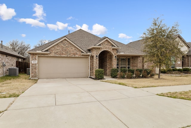 view of front facade with concrete driveway, roof with shingles, an attached garage, central air condition unit, and brick siding