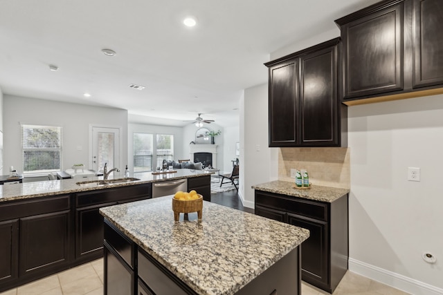 kitchen with a kitchen island, open floor plan, a sink, a fireplace, and stainless steel dishwasher