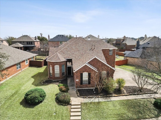 view of front of house featuring brick siding, fence, a front lawn, and roof with shingles