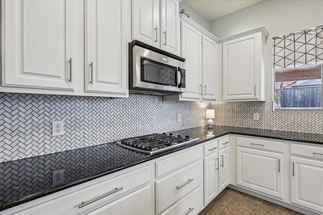 kitchen with tasteful backsplash, dark countertops, appliances with stainless steel finishes, white cabinetry, and tile patterned flooring