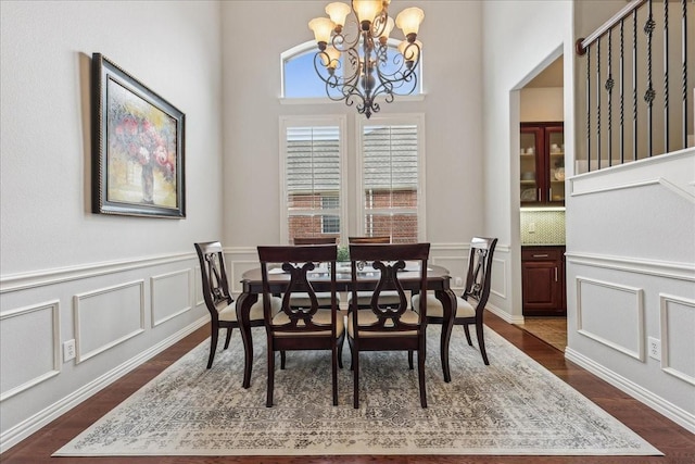 dining space featuring dark wood-style floors, stairway, a notable chandelier, and a decorative wall