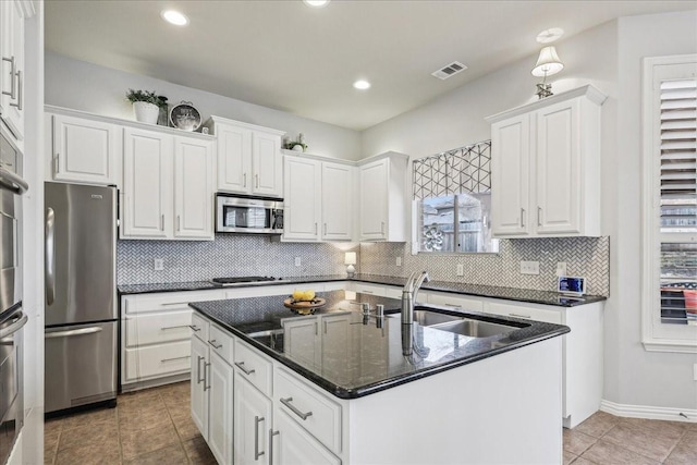 kitchen with a sink, visible vents, white cabinets, appliances with stainless steel finishes, and a center island with sink