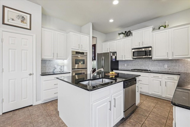 kitchen with a center island with sink, backsplash, appliances with stainless steel finishes, white cabinetry, and a sink