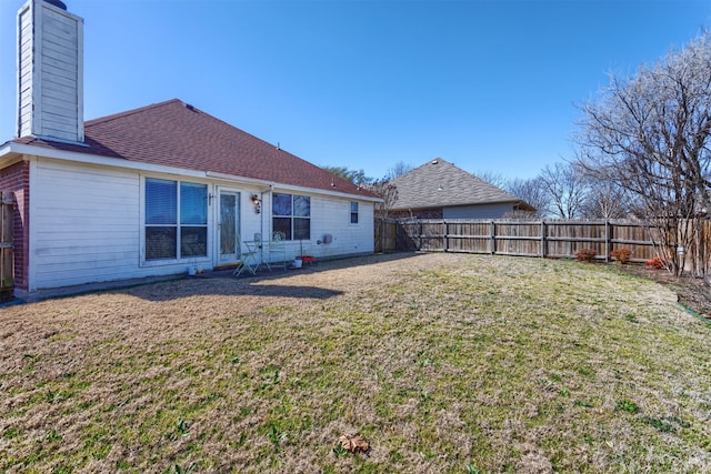 rear view of house with a shingled roof, a fenced backyard, a lawn, and a chimney