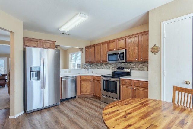 kitchen with a sink, light countertops, light wood-style floors, appliances with stainless steel finishes, and tasteful backsplash