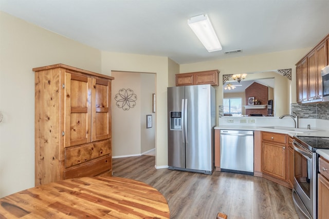 kitchen featuring a sink, stainless steel appliances, light countertops, light wood-type flooring, and backsplash