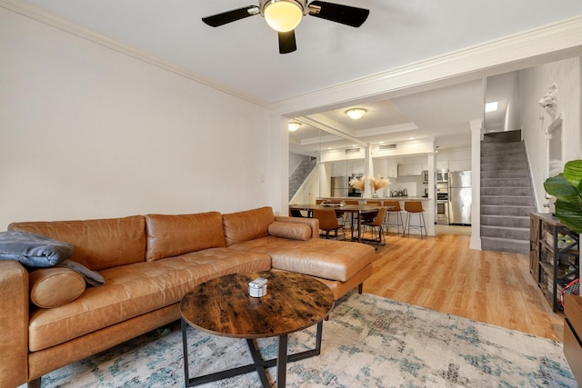 living area with ornamental molding, light wood-type flooring, ceiling fan, and stairway