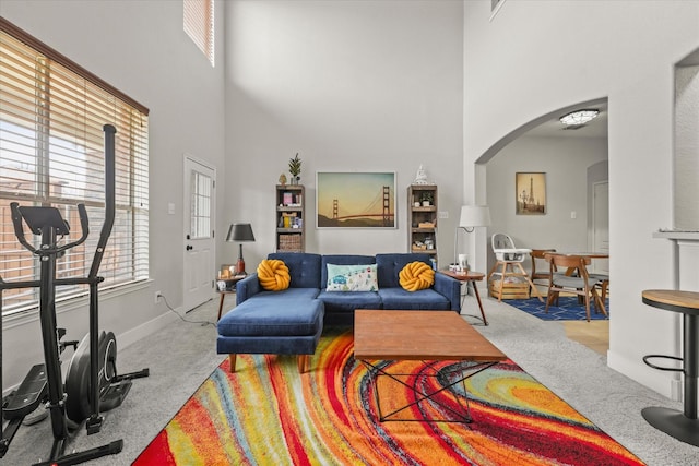 carpeted living area with arched walkways, a high ceiling, and baseboards