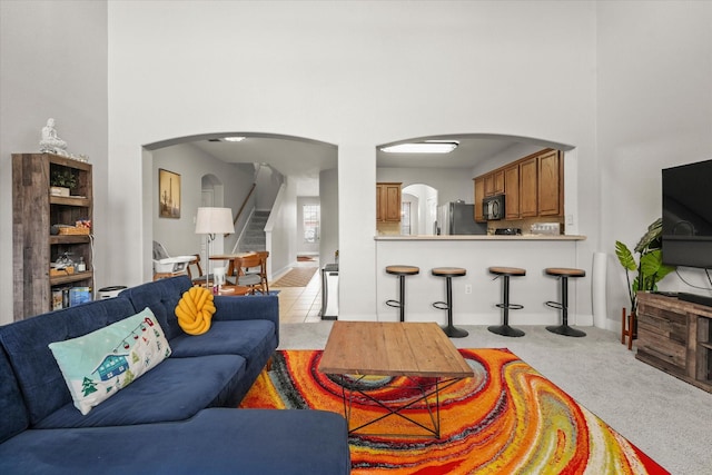 living area featuring arched walkways, a high ceiling, stairs, and light colored carpet