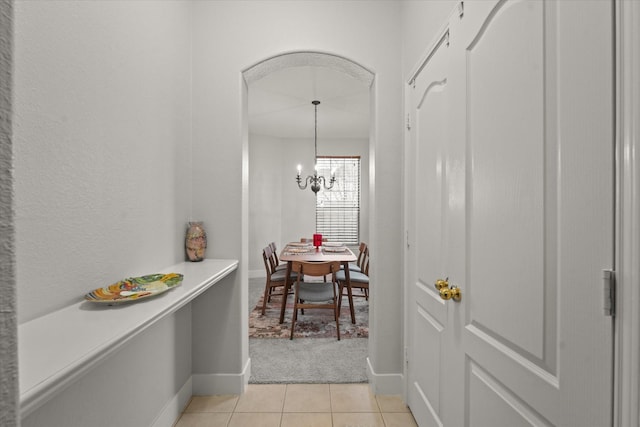 corridor with baseboards, light tile patterned flooring, light colored carpet, and a notable chandelier