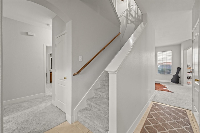 stairs featuring arched walkways, tile patterned flooring, and carpet flooring