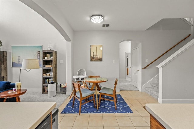 dining space featuring arched walkways, light tile patterned floors, visible vents, light carpet, and stairs