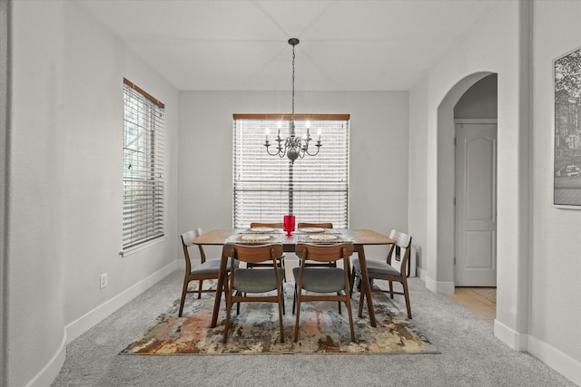 carpeted dining space with arched walkways, baseboards, and an inviting chandelier