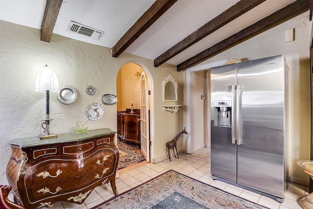 hallway with light tile patterned floors, visible vents, arched walkways, a textured wall, and vaulted ceiling with beams