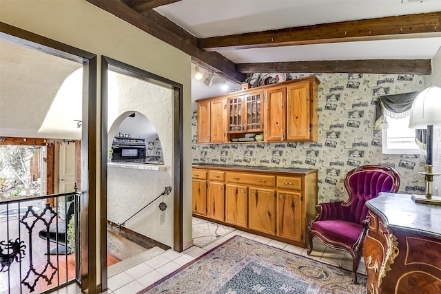 kitchen with lofted ceiling with beams, arched walkways, light tile patterned flooring, brown cabinetry, and glass insert cabinets