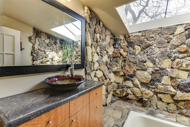 bathroom with stone finish flooring, a skylight, a bathtub, and vanity