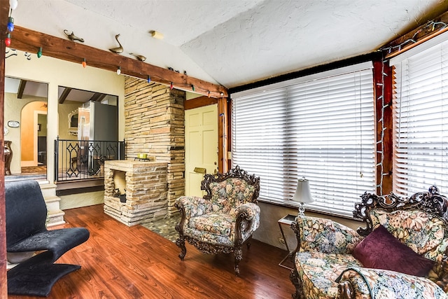 living area featuring lofted ceiling, wood finished floors, a textured ceiling, and arched walkways