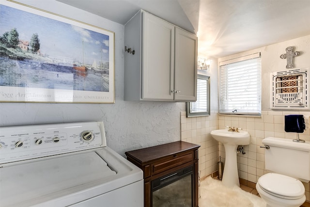 interior space with tile walls, toilet, washer / clothes dryer, heating unit, and a sink