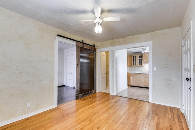 unfurnished room with ceiling fan, light wood-style flooring, baseboards, and a barn door