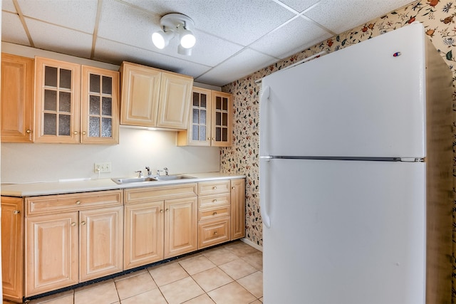 kitchen with light tile patterned flooring, a paneled ceiling, a sink, freestanding refrigerator, and glass insert cabinets