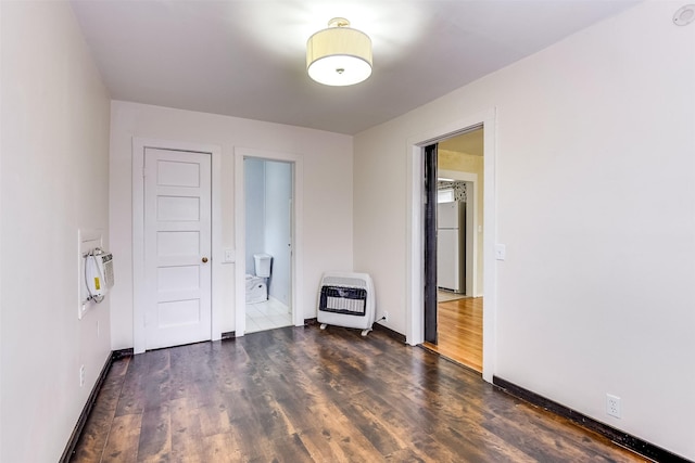 unfurnished room featuring heating unit, baseboards, and wood finished floors