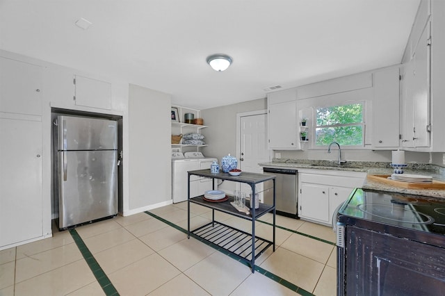 kitchen with light tile patterned floors, stainless steel appliances, washing machine and dryer, white cabinetry, and a sink